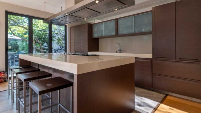 Luxury Polyform Walnut Kitchen with Pocket Doors and Matching Island - Gaggenau Verenna & Foster Appliance – Sand Coloured Corian Worktops