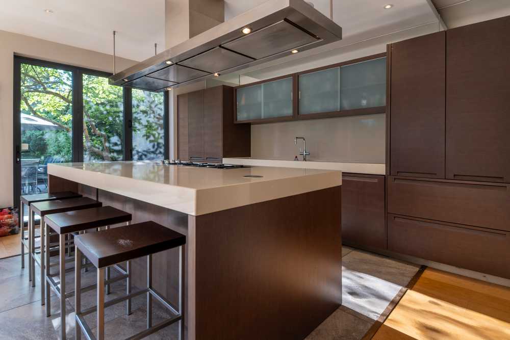 Luxury Polyform Walnut Kitchen with Pocket Doors and Matching Island - Gaggenau Verenna & Foster Appliance – Sand Coloured Corian Worktops
